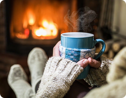 Cozy winter scene: Person savoring a hot cup of coffee while gazing at a crackling gas fireplace