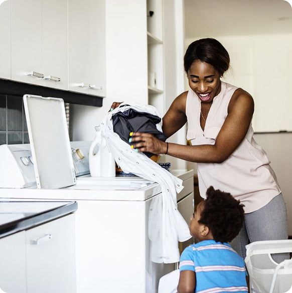 Joyful mother and son working together, smiling as they load clothes into the washing machine
