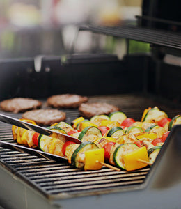 Colorful vegetable skewers and sizzling grilled hamburgers cooking on a barbecue grill