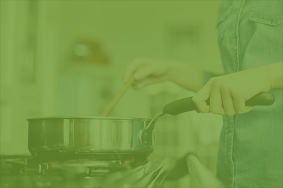 Person cooking on gas cooktop, using stainless steel skillet and wooden spoon