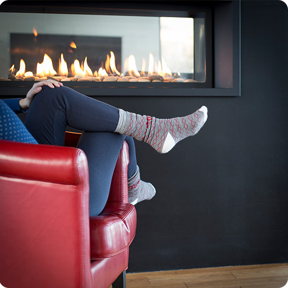 Stylishly crossed legs in red chair by a see-thru gas fireplace, creating a cozy and fashionable ambiance