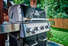 BroilKing Baron 440 Pro: Closeup of the grill with mouthwatering smoke billowing out, set against a picturesque outdoor backdrop