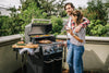 Couple grilling with joy on the BroilKing Baron 440 Pro, savoring food and wine in a delightful outdoor setting