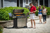 Man grilling on BroilKing Baron S 590 IR grill in red shirt; two women with drinks approaching