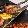 BroilKing Baron S 590 IR grill cooking sausage and pineapples on top shelf with grill tongs